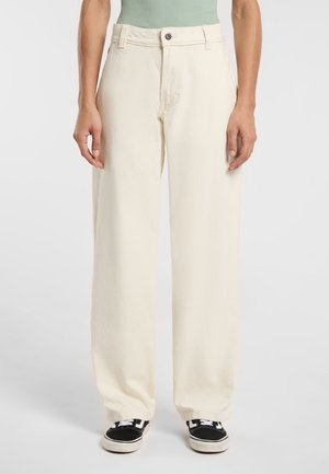 Pantaloni a gamba larga color crema realizzati in materiale morbido, con chiusura a bottone e tasche frontali, abbinati a sneakers nere.