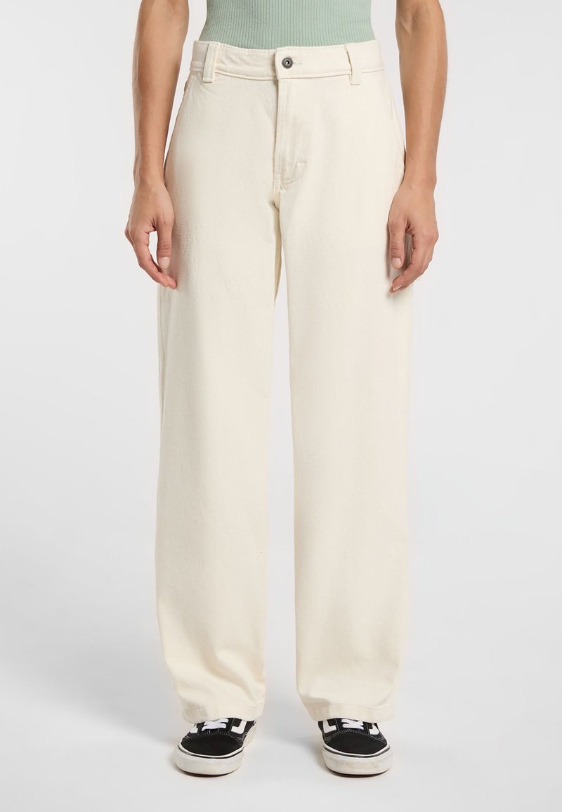 Pantaloni a gamba larga color crema realizzati in materiale morbido, con chiusura a bottone e tasche frontali, abbinati a sneakers nere.