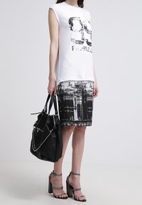 T-shirt grafico bianco con stampa nera, abbinato a una gonna a metà polpaccio a motivi bianchi e neri, borsa nera e sandali con tacco chunky.