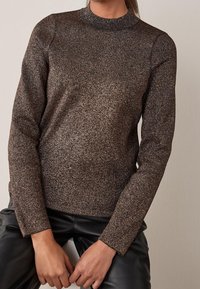 Maglione lungo marrone a maniche lunghe con collo alto, caratterizzato da un discreto motivo a macchie e un design aderente, abbinato a pantaloni in pelle nera.