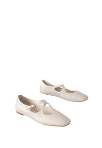 Fehér bőrbalerinacipő kivágott mintával és kis pánttal. Oldalain finom szegecses díszítéssel és lapos talppal rendelkezik.