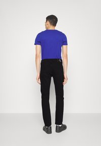 Blauw T-shirt met korte mouwen, gecombineerd met zwarte slim-fit jeans. Het T-shirt heeft een ronde hals; de jeans hebben een logo detail op de achterzak. Zwarte schoenen.