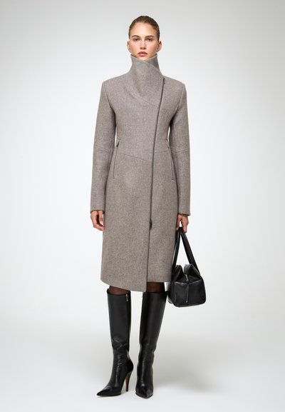 Cappotto di lana grigio con colletto alto e zip asimmetrica, abbinato a stivali neri in pelle con tacco a stiletto al ginocchio e una borsa nera.