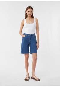 Niebieskie szorty dżinsowe z postrzępionym dołem, wysokim stanem i bocznymi kieszeniami, w zestawie z białym topem na ramiączkach i sandałami na paski.