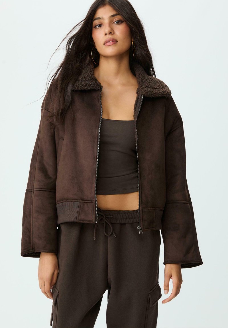 Giacca cropped in finta suede marrone con colletto in pelliccia texturizzata marrone, chiusura con zip, maniche lunghe svasate e tasche laterali.