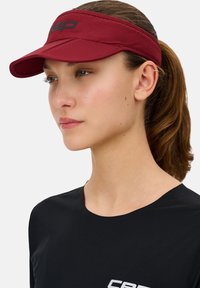 Red visor cap with a textured finish and a black logo. Paired with a black, short-sleeve, ribbed top featuring a white printed logo.