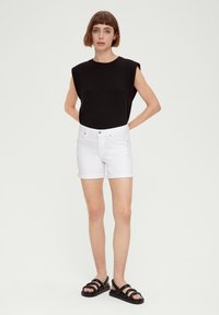 Zwart kortemouwen top met schoudervullingen, gecombineerd met witte denim shorts en zwarte sleehakken. Eenvoudige, casual zomeroutfit.