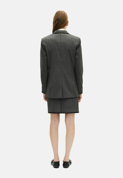 Op maat gemaakte grijze krijtstreep suit met een blazer en rok. De blazer heeft gestructureerde schouders, terwijl de rok knielang is.