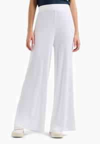 Pantaloni bianchi a gamba larga con una texture a costine e vita elasticizzata, abbinati a sneaker bianche, che enfatizzano un fit rilassato e un design fluido.