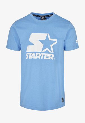 Himmelblaues T-Shirt mit kurzen Ärmeln aus Baumwolle, das auf der Vorderseite ein großes weißes "S" und ein Sternlogo zeigt. Am Saum befindet sich ein kleines schwarzes Markenetikett.