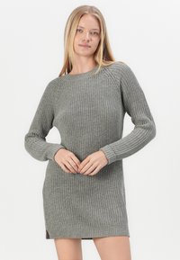 Szürke kötött pulóverruha bordázott textúrával, hosszú ujakkal és kerek nyakú kivágással. Oldalsó hasadékokkal a szegénynél a könnyebb mozgás érdekében.