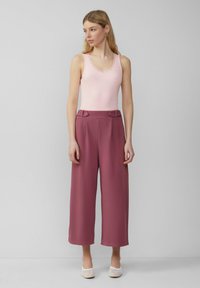 Débardeur rose à côtes avec dentelle, associé à un pantalon large taille haute dans un mauve atténué, agrémenté de boutons à la taille.