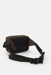 Bolso de hombro de tela marrón con forma rectangular, que presenta una base negra y un detalle a cuadros. Correa ajustable con hebilla de plástico negra.