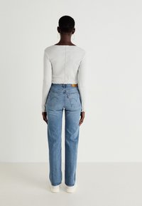 Top de manga larga de canalé gris claro con diseño corto, combinado con jeans de mezclilla azules que presentan un acabado desgastado, corte recto y bolsillos traseros.