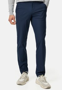 Navy blue, slim-fit trousers made from lightweight fabric; features a flat front, side pockets, and are paired with beige sneakers.
