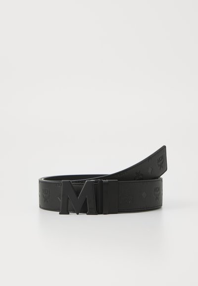 Svart läderbälte med präglat mönster och en blank svart metallspänne med ett "M"-logo. Slät textur med en elegant design.
