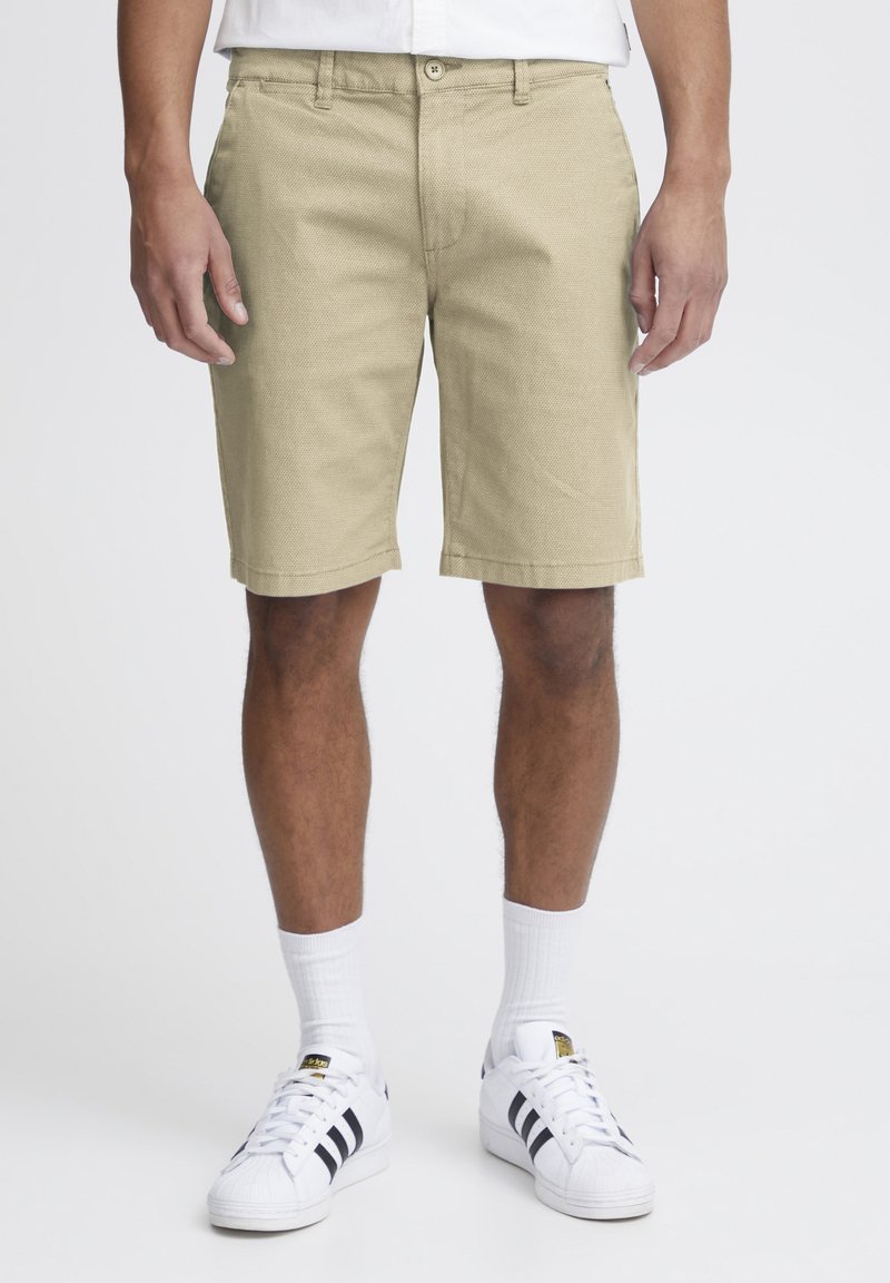 Shorts kaki en tissu texturé, avec une coupe standard, des passants de ceinture et un bouton de fermeture, dans un style épuré et simple.