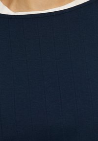 Marineblauw topje met ribbelstructuur, ronde witte kraag en verticale strepen die over de stof lopen. Zacht, rekbaar materiaal.
