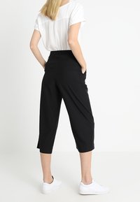 Zwarte cropped broeken met een hoge taille en zijzakken, gecombineerd met een witte blouse met korte mouwen en witte sneakers. Glad stoffen textuur.