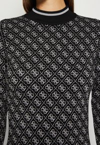 Pull noir en tricot avec un motif de losanges blancs répétés, un col rond côtelé noir avec des accents gris.