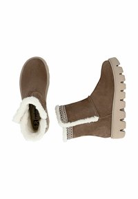 Botas de tobillo de ante marrón con un forro de piel sintética blanca, costuras decorativas en el puño y una suela gruesa y robusta de color beige.