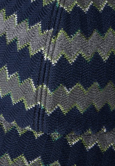 Gros plan d’un tissu tricoté avec un motif en zigzag bleu marine, gris et couture vert clair.
