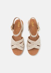 Beige lær sandaler med kryssende stropper, åpen tå og justerbar ankelspenne. Brun polstret innersåle med perforeringer for pusteevne.