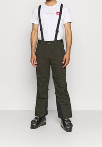 Gröna skidbyxor med justerbara svarta hängslen, som har dragkedjefickor och förstärkta svarta paneler vid anklarna.