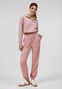 Pull en rose clair à zip 1/4 avec des manches longues et un pantalon assorti. Tissu doux, taille élastique et chevilles côtelées. Style athlétique décontracté.