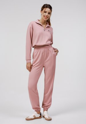 Lys pink 1/4 zip pullover med lange ærmer og matchende joggers. Blødt stof, elastisk talje og afsluttede ankle. Afslappet atletisk stil.