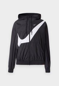 Svart vindjacka med en stor vit Nike Swoosh-logotyp. Har huva, framfickor, elastiska muddar och dragsko i fållen.