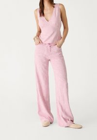 Femme portant un haut sans manches rose brodé de fleurs et un pantalon large assorti avec des chaussures à enfiler en osier beige.