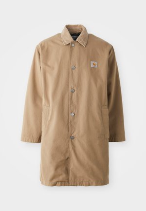 Beige lange jas van duurzame stof, met een corduroy kraag, metalen drukknoopsluiting en twee zijzakken. Carhartt logo patch op de borst.