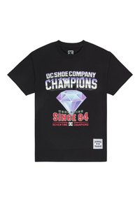Black cotton t-shirt featuring bold graphic print with "DC Shoe Company," a diamond shape, and "Champions" text in various colors.