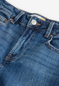 Jeans in denim a vita alta di colore blu scuro con una trama scolorita, caratterizzati da una chiusura con bottone metallico, rivetti in rame e tasche cucite.