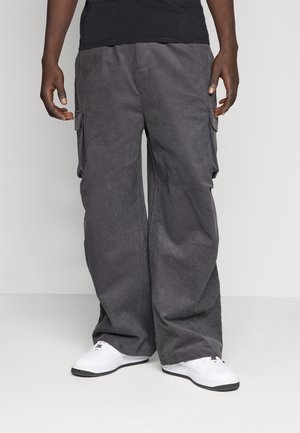 Grijze corduroy cargobroek met een losse pasvorm, voorzien van zijzakken en een textuurpatroon. Gecombineerd met witte sneakers.