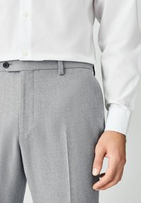 Grijze op maat gemaakte broek met een getextureerde afwerking, voorzien van vlakke zakken aan de voorkant en lussen voor een riem, gedragen met een wit shirt met lange mouwen.