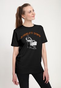Sort t-shirt med teksten "BUBBLE'S DEPO" i orange, med et grafisk motiv af en person, der skubber en indkøbsvogn.