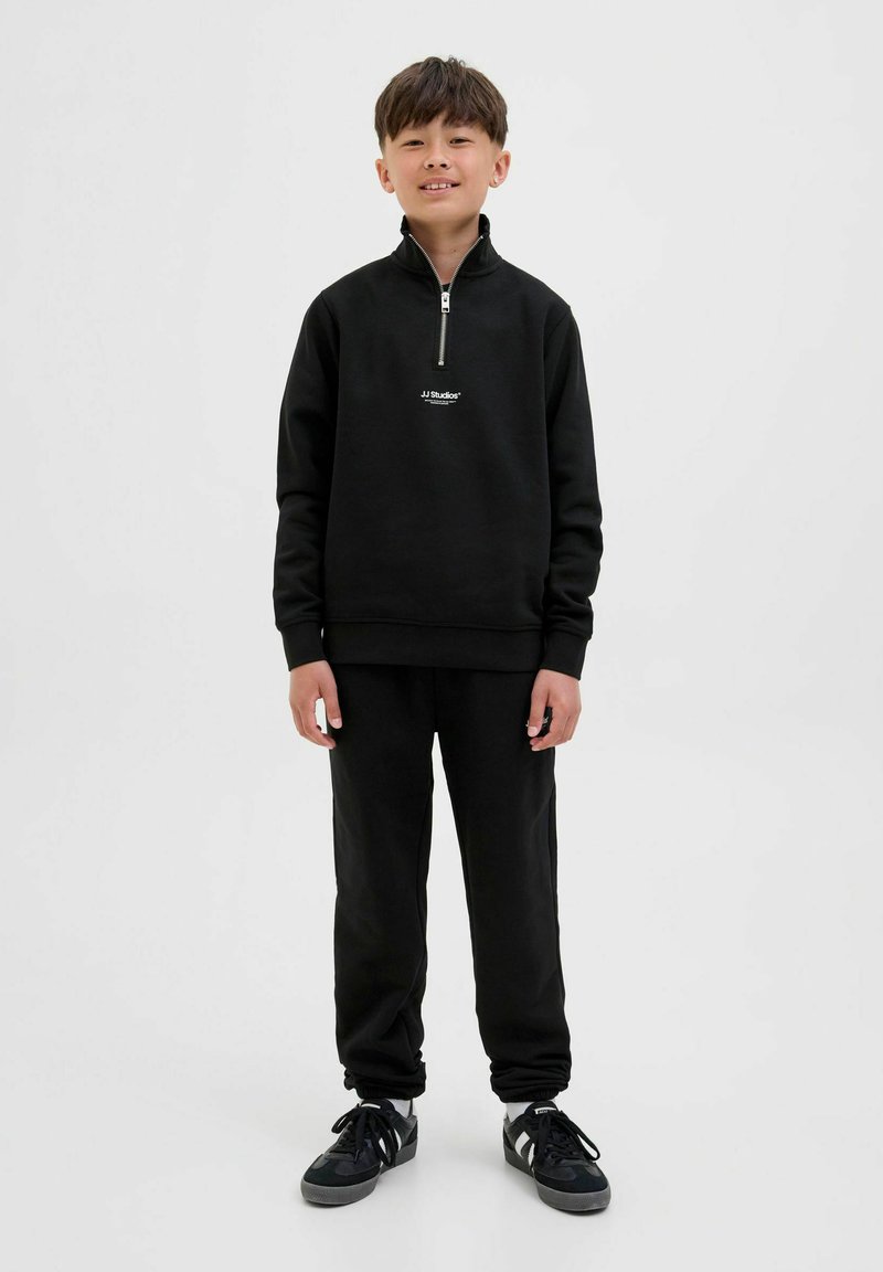 Svart zip-up sweatshirt med logotyp, parat med matchande svarta byxor. Slät tyg, avslappnad passform, ribbade muddar och subtila detaljer.