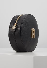 Borsa rotonda nera in pelle con superficie texturizzata, zip dorata e hardware di accentuazione con un dettaglio del logo sul fronte.