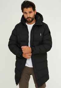 Black padded winter coat with a hood, zippered front, two chest pockets, and elastic cuffs. Smooth texture with a glossy finish.