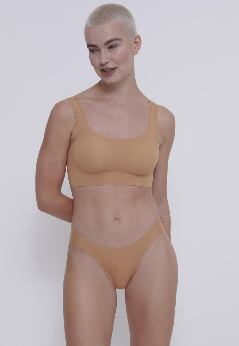 Bralette senza cuciture color terra con spalline larghe e materiale morbido e elastico. Abbinato a un perizoma a vita bassa coordinato, entrambi hanno una texture liscia.