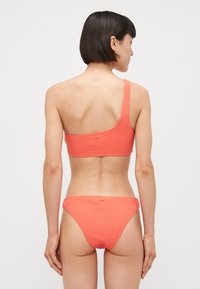 Bikini corallo a spalla unica con tessuto testurizzato. Il top presenta una larga tracolla, mentre il fondo ha un design semplice a vita bassa.