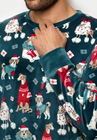 Zielony polarowy sweter z festywnymi wzorami psów i owiec w czapkach Mikołaja. Okrągły dekolt i długie rękawy. Miękka, strukturalna tkanina.