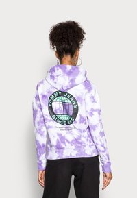 Purple tie-dye hoodie with a large graphic logo on the back, featuring a globe design. Material appears soft with a relaxed fit.