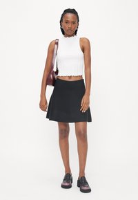 Fehér bordázott crop top, fodros szegéllyel, fekete bővülő szoknyával és fekete platform loaferekkel párosítva. Bordó táska oldalán hordva.