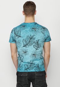 Tūris zils T-krekls ar melniem ziedu un lapu rakstiem, īsām piedurknēm un apaļu kakla izgriezumu, veikts no mīkstas, strukturētas auduma.