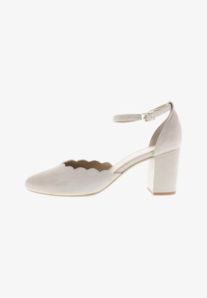 Beige suede block-heeled shoe with scalloped design on the upper edge and an adjustable ankle strap. Flat sole, smooth texture.