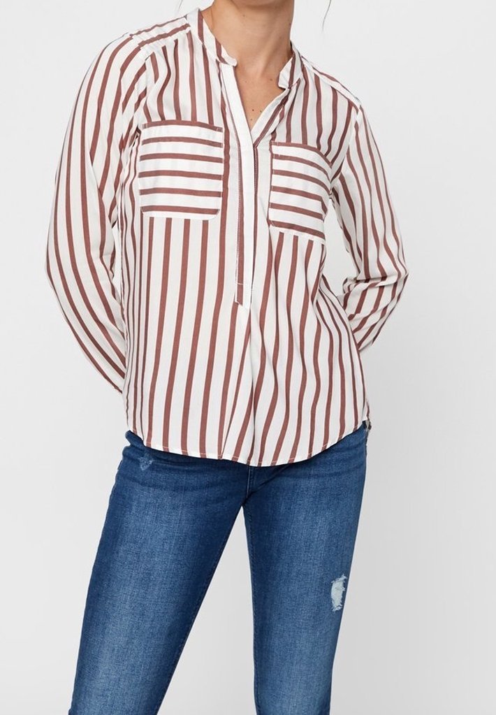 Vit och brunrandig långärmad skjorta med två bröstfickor, delvis knäppning och avslappnad passform, bärs med blå jeans.