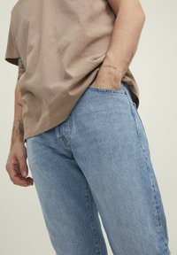 Light blue denim jeans with a straight cut, featuring a classic five-pocket design and subtle stitching details. Paired with a brown cotton t-shirt.